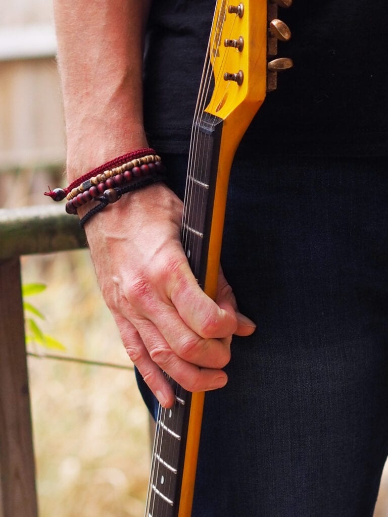 Trend Him stacking bracelet on a man's wrist. Man is also holding the neck of a guitar